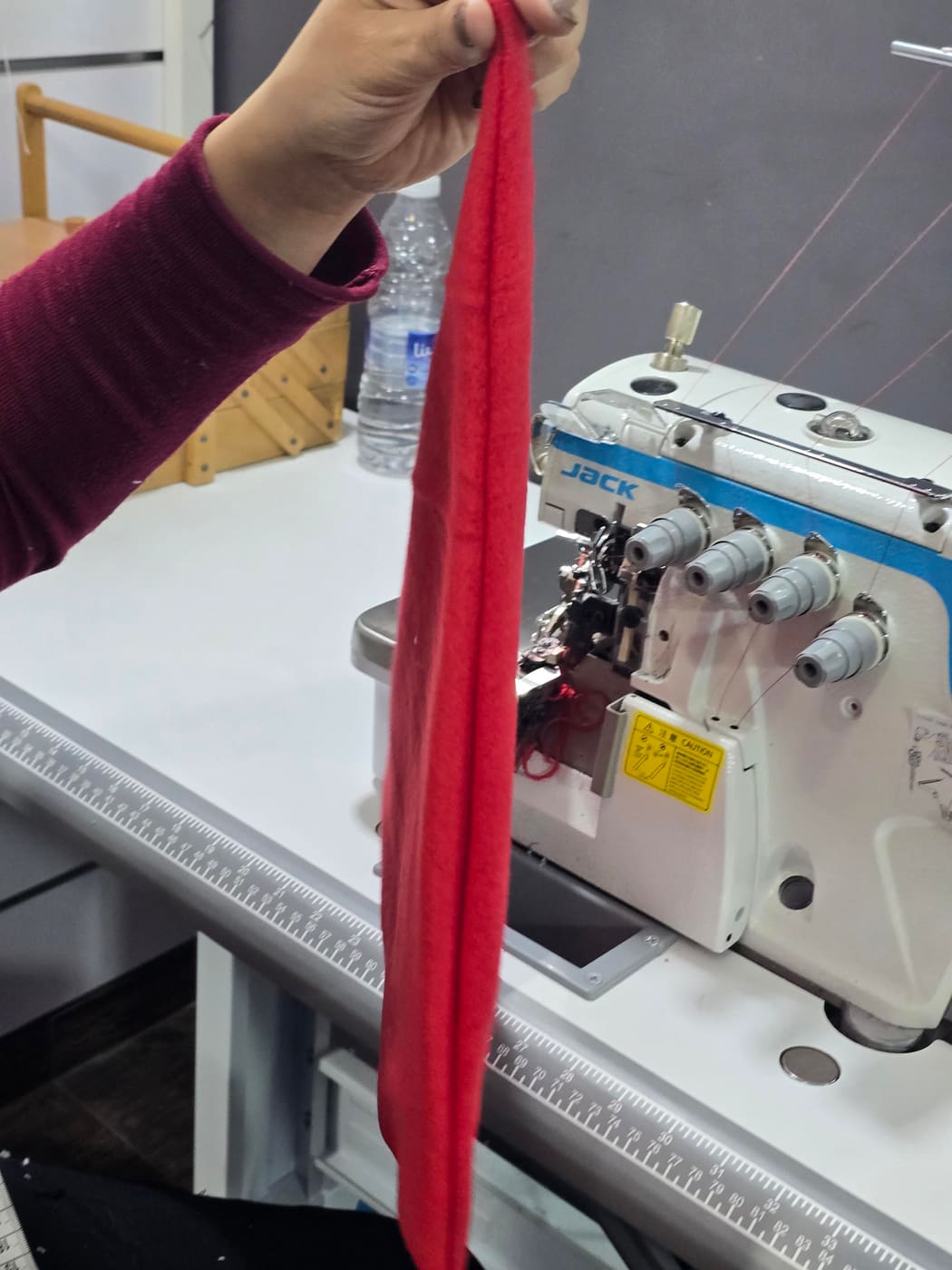 A tailor checking a red knit garment at an overlock machine at Younes Tailor